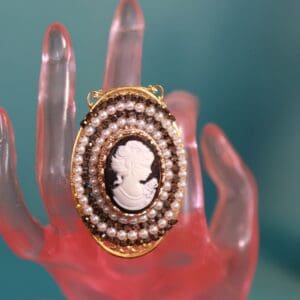 A hand holding a pearl and cameo ring.
