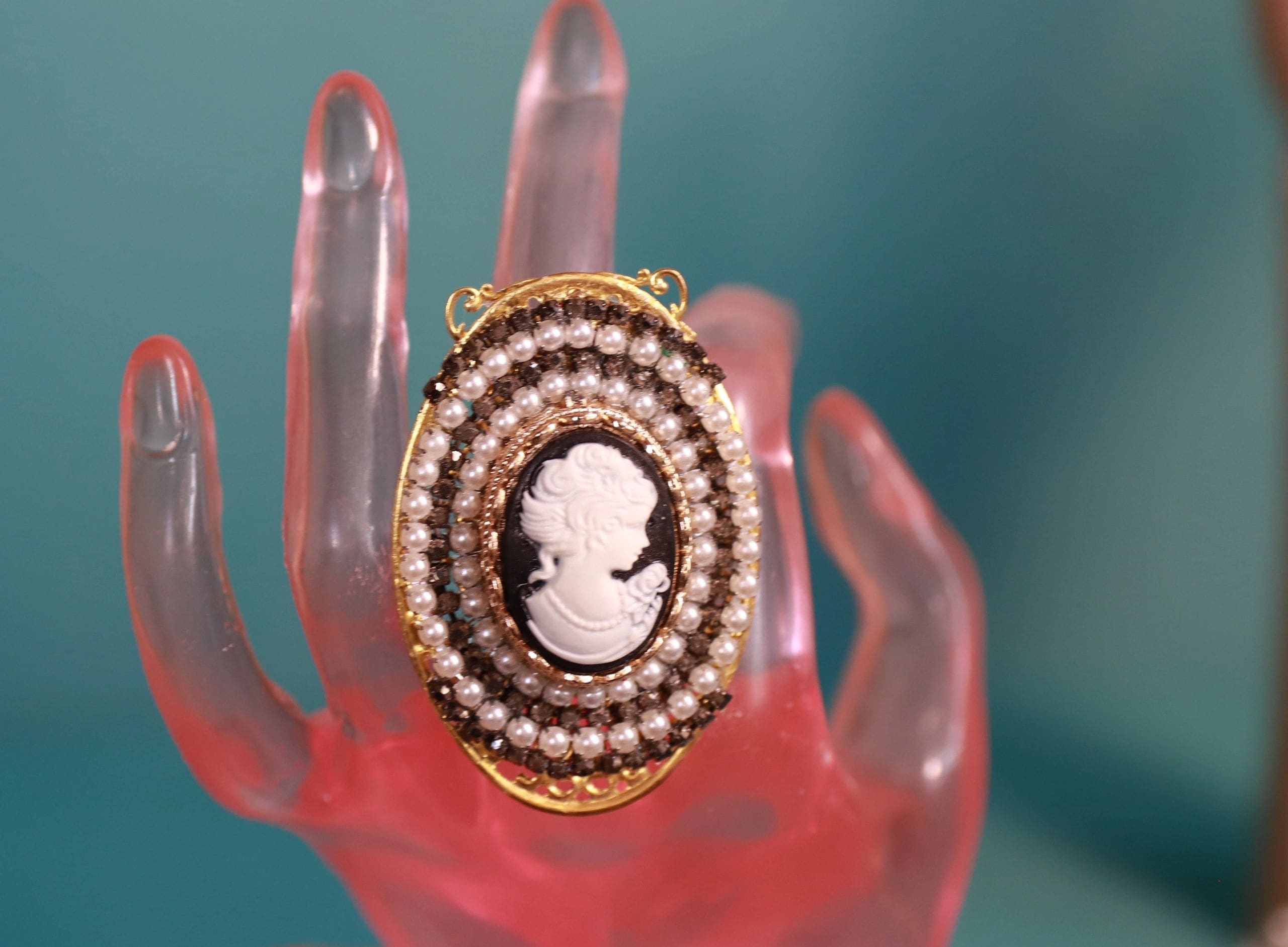 A hand holding a pearl and cameo ring.