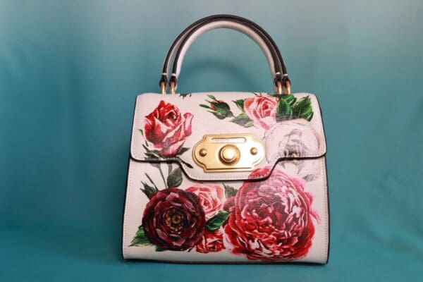 A white purse with red and pink flowers on it.