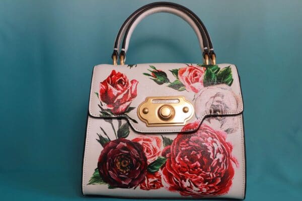 A white purse with red and pink flowers on it.