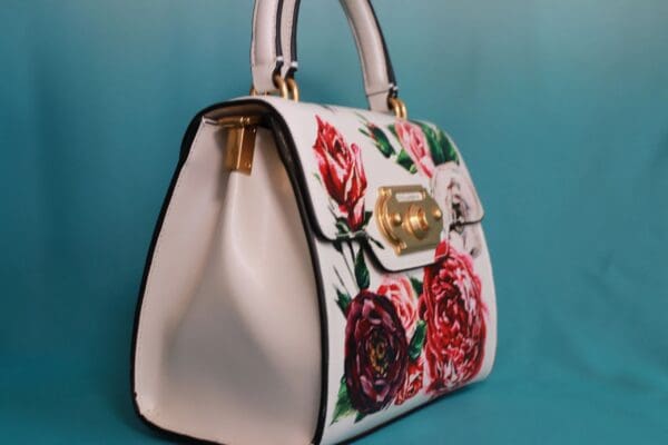A white purse with red and pink flowers on it.