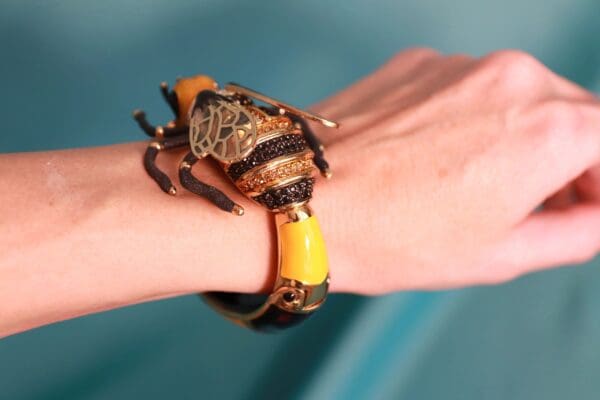 A person wearing a yellow and black bracelet with a bug on it.