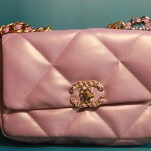 A pink purse with gold chain handles and a clasp.