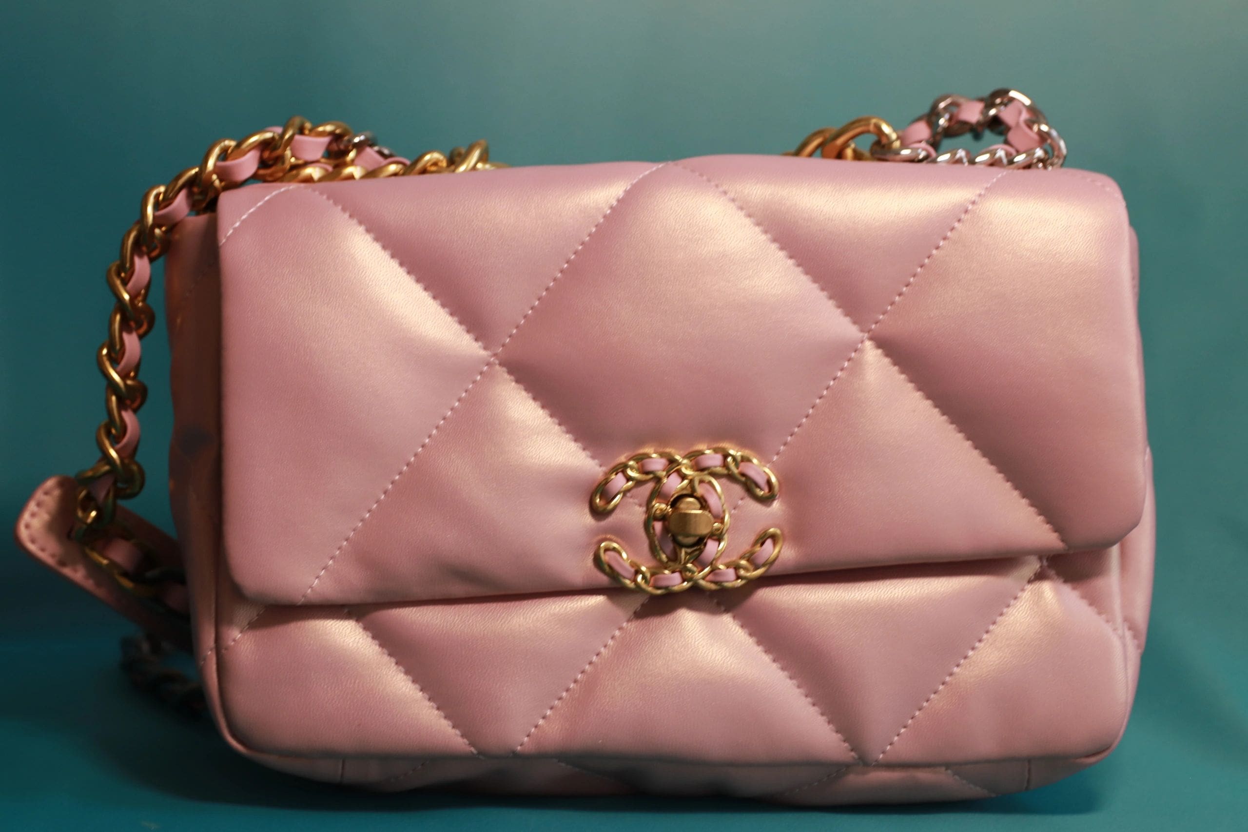 A pink purse with gold chain handles and a clasp.
