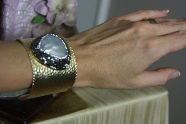 A person wearing a gold bracelet with a stone on it.