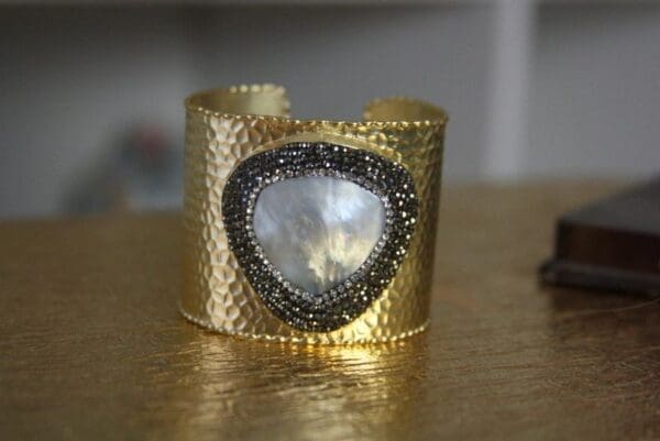 A gold cuff bracelet with a heart shaped stone.