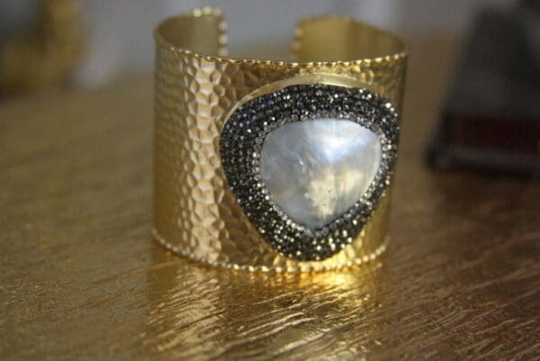 A gold bracelet with a heart shaped stone on it.