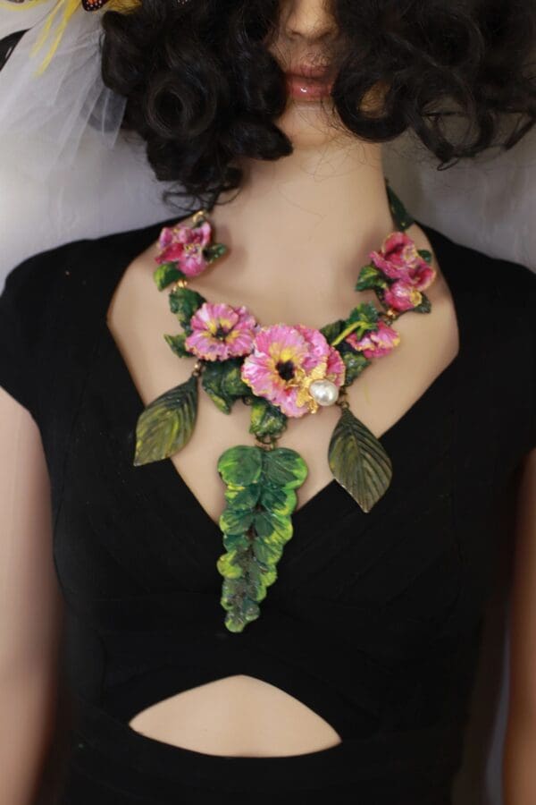 A woman wearing a necklace with pink flowers and green leaves.