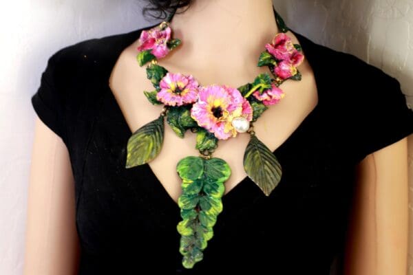 A woman wearing a necklace with pink flowers and green leaves.