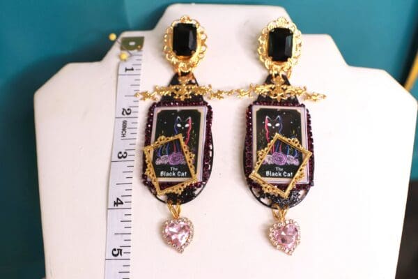 A pair of earrings with a large black frame and pink heart.