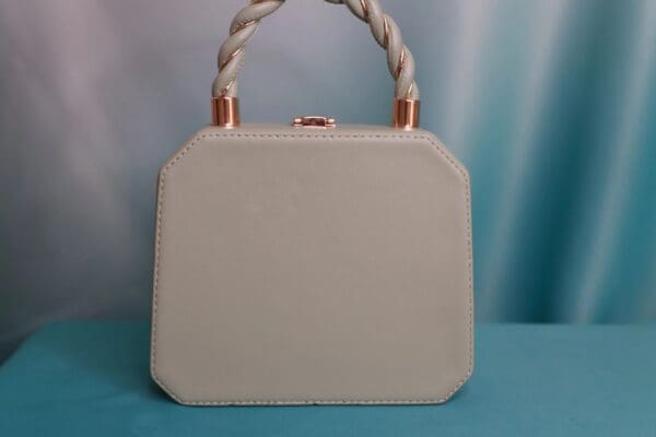A white purse with a rope handle on top of a blue table.