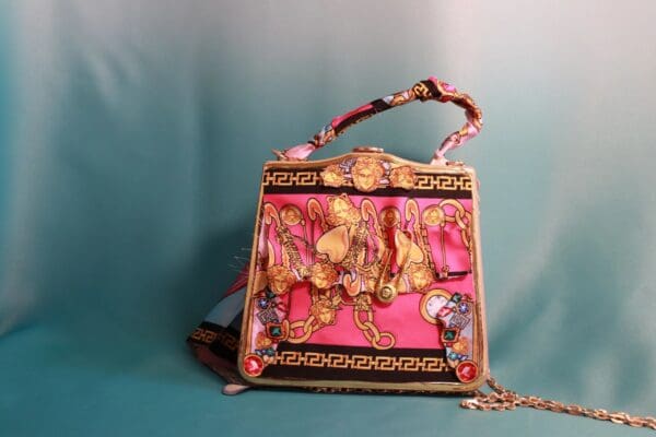 A pink purse with gold chains and flowers on it.