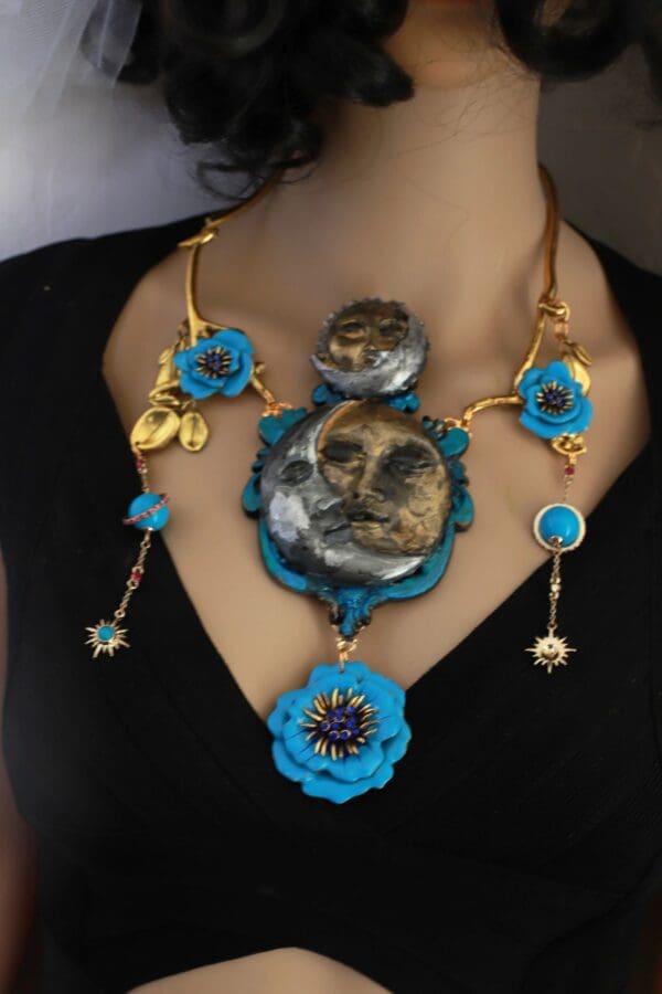 A woman wearing a necklace with blue flowers and gold chains.