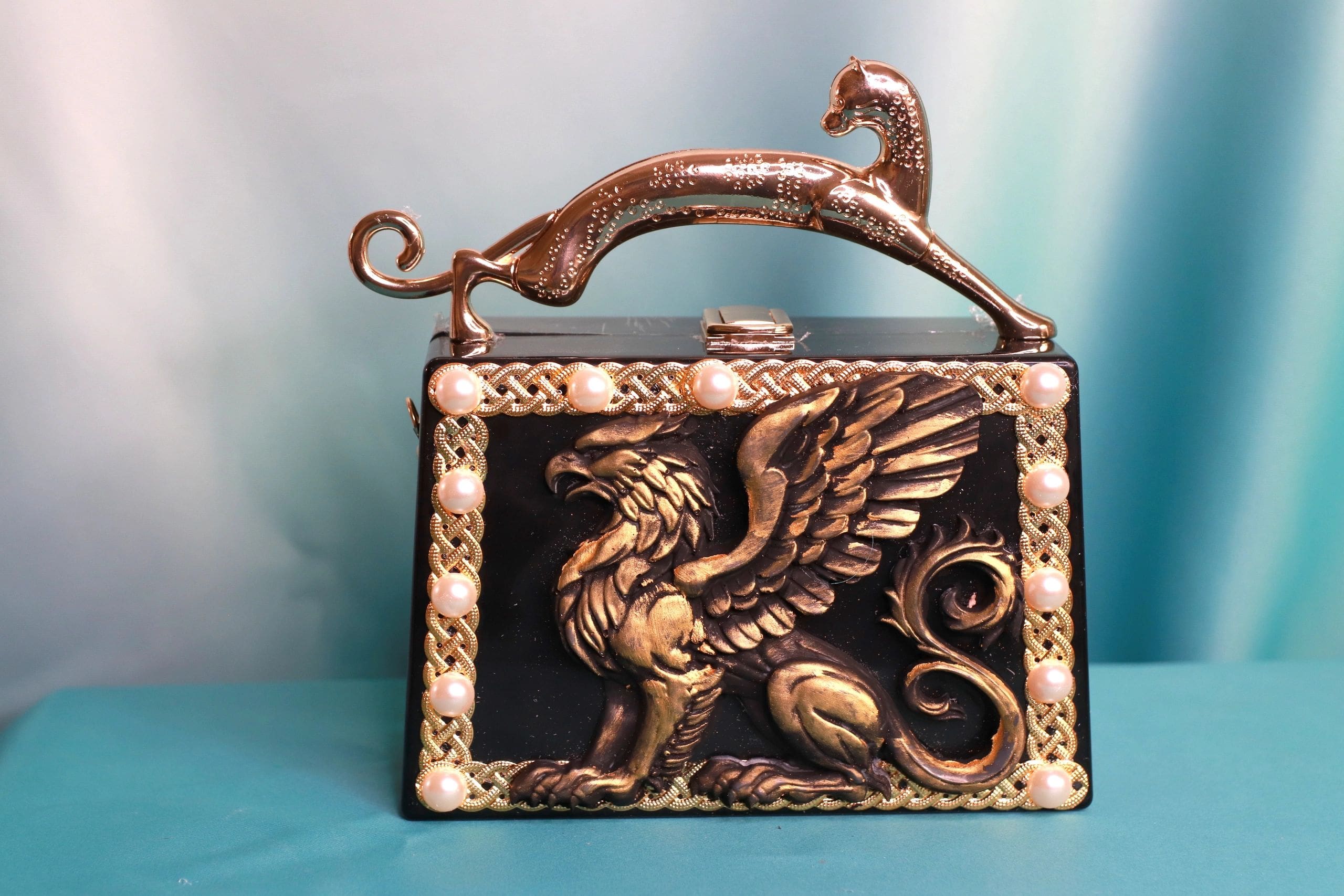 A purse with a metal handle and a picture of a griffin.