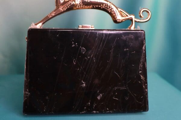 A black purse with a gold handle and a cat on it.