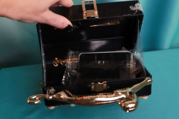 A black purse with gold handles and a phone in it.