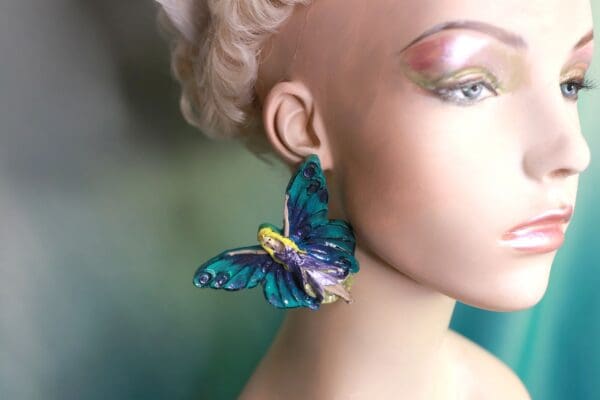 A woman wearing blue butterfly earrings with yellow accents.