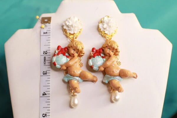 A pair of earrings with cherubs and flowers on them.