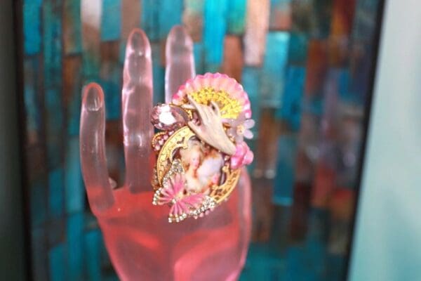 A pink hand with a colorful ring on top of it.