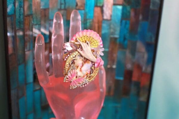 A pink hand with a colorful ring on top of it.
