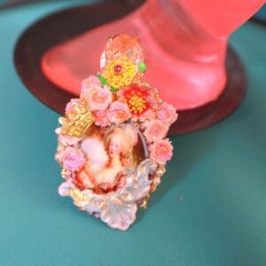 A pink vase with flowers on it and a red hat