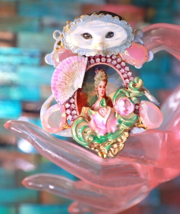 A hand holding a pink and green cat ornament.