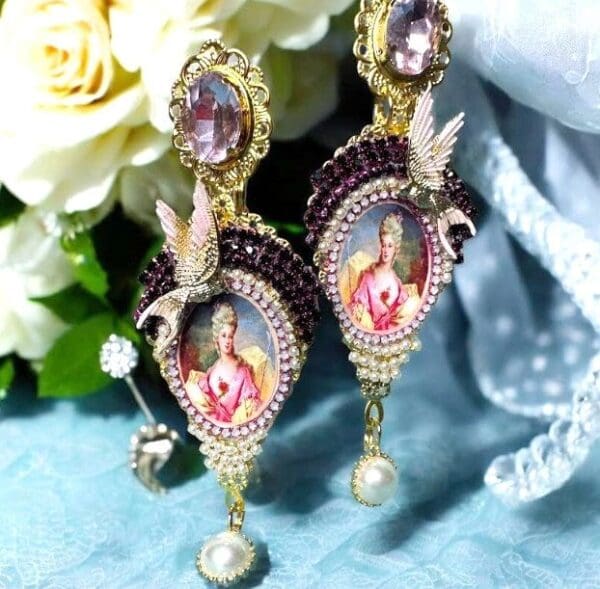 A pair of earrings with pictures and jewels on them.