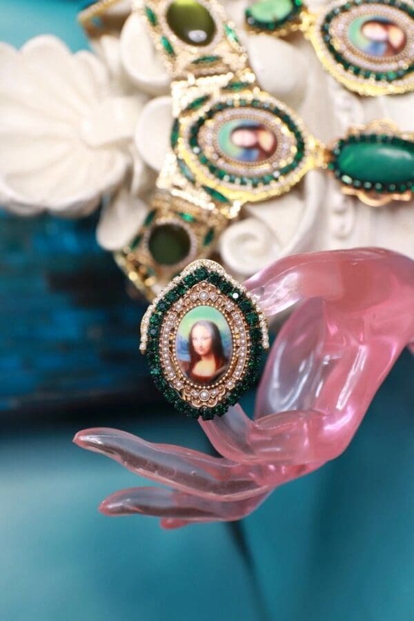 A pink hand holding a green and white necklace.