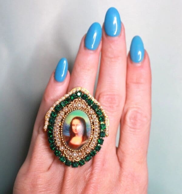 A woman 's hand with blue nails and a ring on her finger.