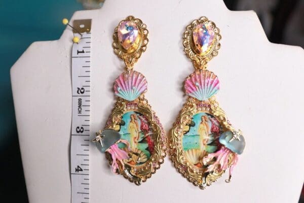 A pair of earrings with mermaids and shells on them.