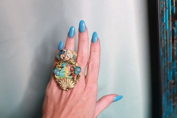 A woman 's hand with blue nails and a ring on her finger.