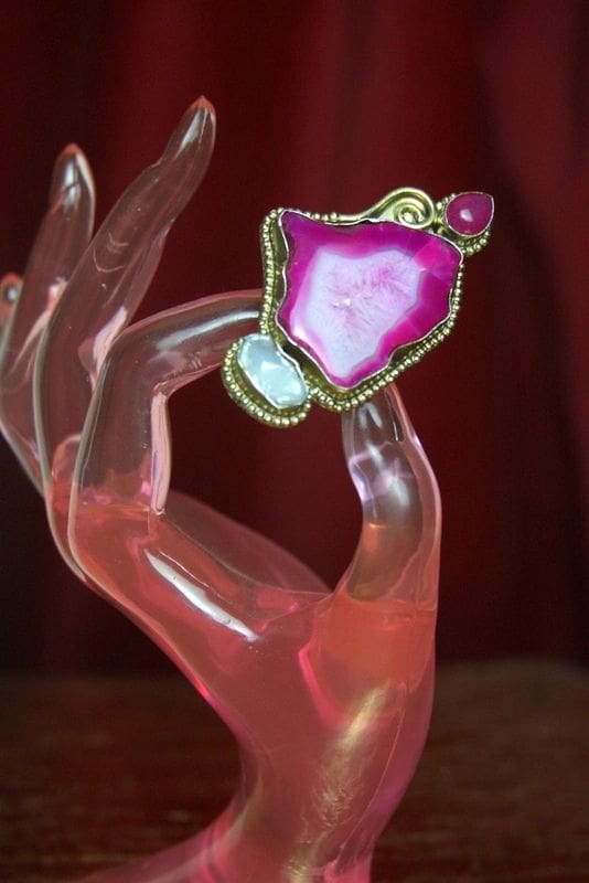 A pink hand holding an agate slice with a gold frame.