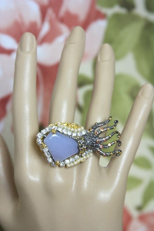 A hand wearing a ring with beads and stones