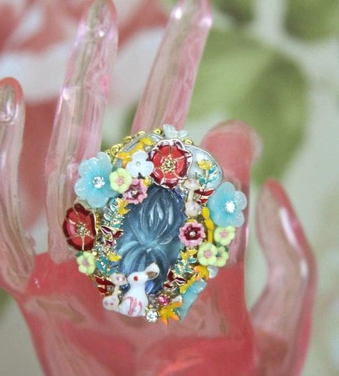 A pink hand with a blue and white flower ring on it.