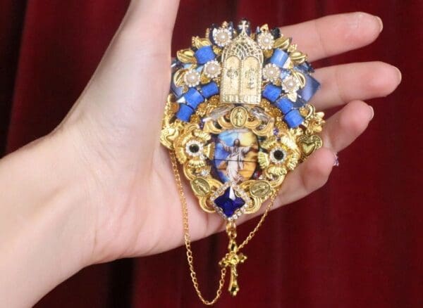 A hand holding a blue and gold piece of jewelry.