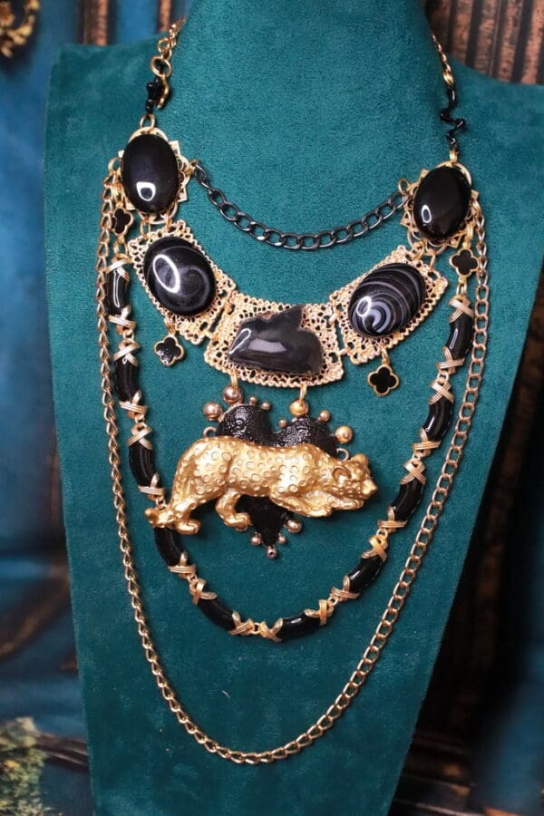 A necklace with black and gold beads, chains and a bear.