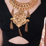 A woman wearing a necklace with tassels and a lion head.