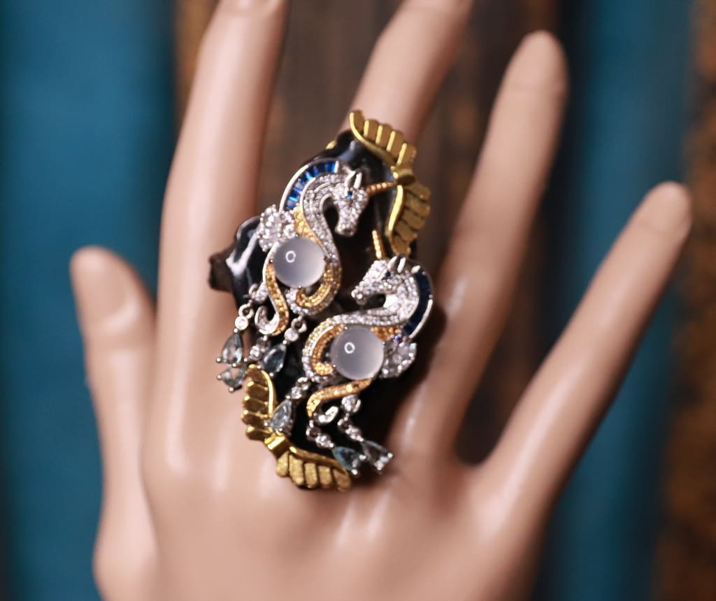 A hand wearing a ring with gold and silver flowers.