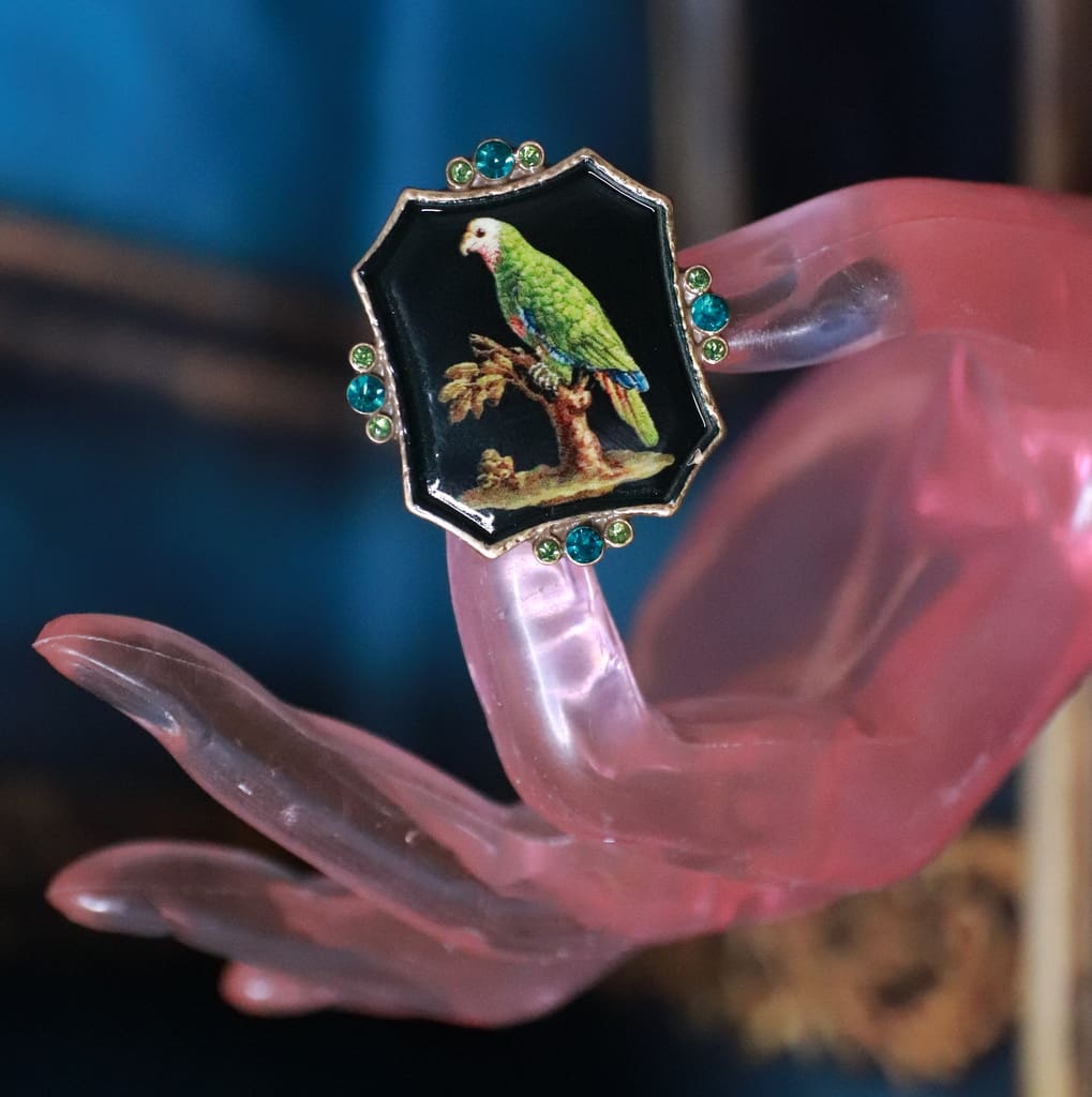 A hand holding a ring with a parrot on it.