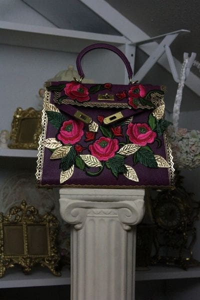 A purple purse with roses on it sitting on top of a pillar.