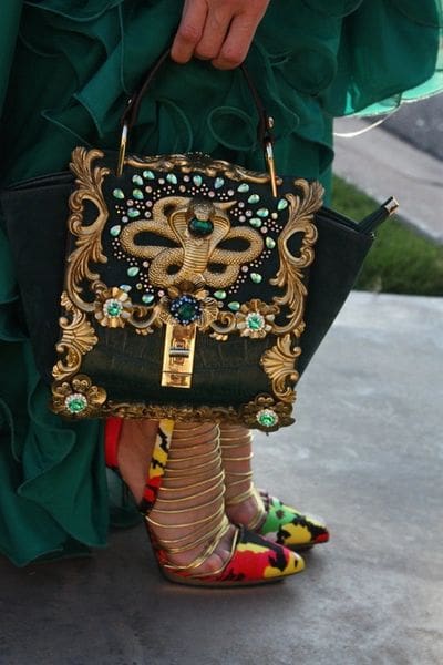 A woman holding an ornate purse on top of her dress.