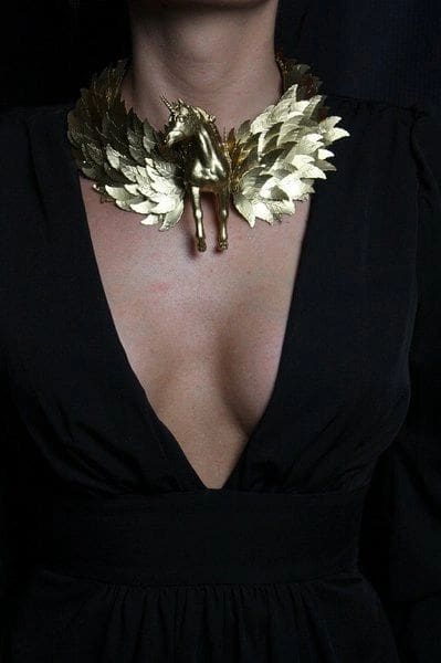 A woman wearing a black dress and gold leaf necklace.