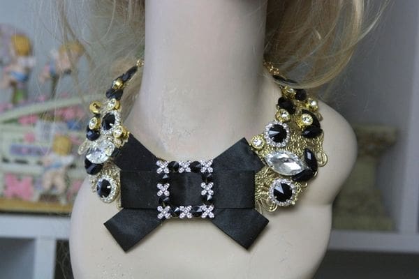 A black bow necklace with gold and silver beads.