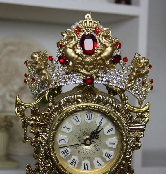 A gold clock with red jewels on top of it.