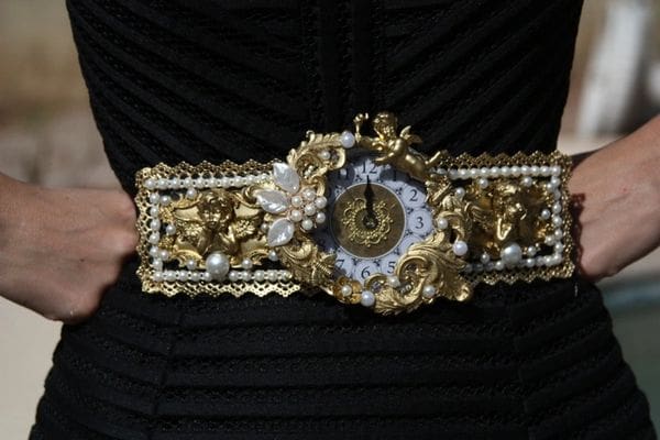 A woman holding onto a gold and pearl bracelet with a clock