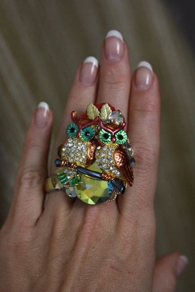 A woman is holding her ring with two owls on it.