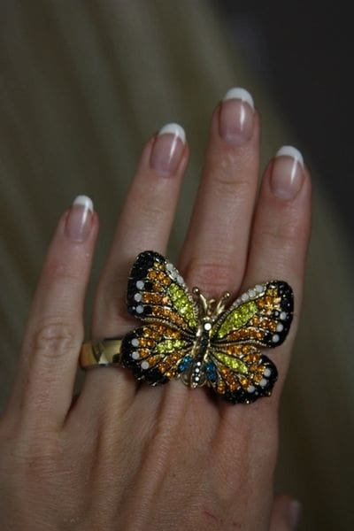 A woman 's hand with french manicure and butterfly ring.