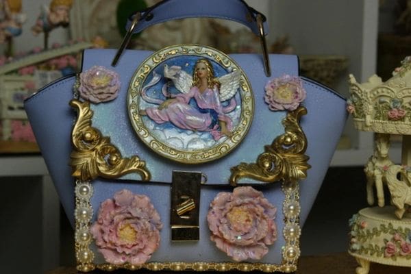 A blue purse with pink flowers and a picture of an angel.