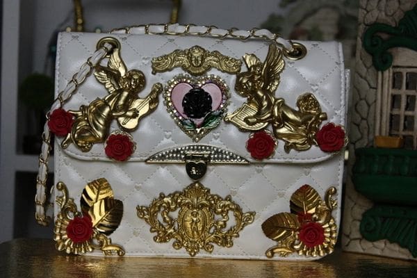A white purse with gold and red embellishments.