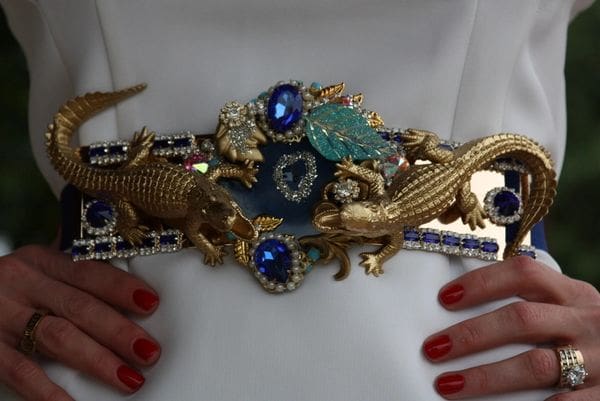 A woman wearing a white dress with red nails and a blue belt.